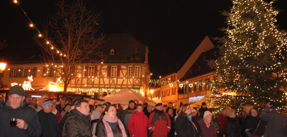 Menschen stehen neber einem Weinnachtsbaum im Dunklen