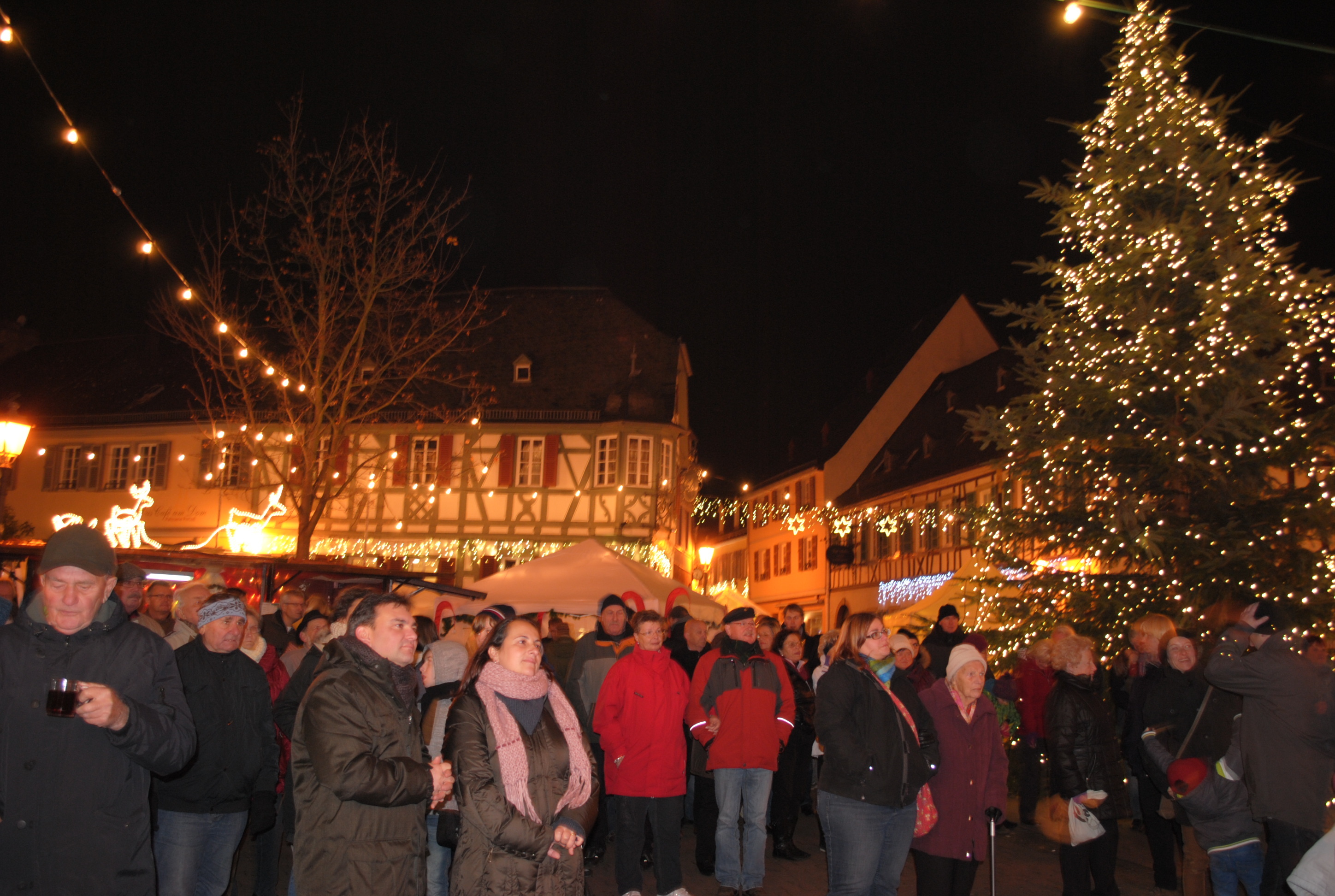 Menschen stehen neber einem Weinnachtsbaum im Dunklen