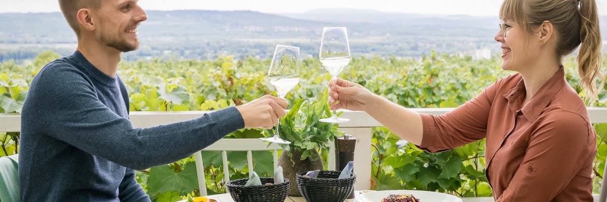 ein Paar stößt mit Weingläsern an, mit Weinbergen im Hintergrund