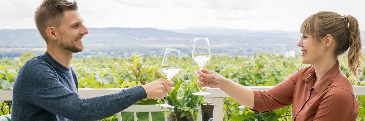 ein Paar stößt mit Weingläsern an, mit Weinbergen im Hintergrund