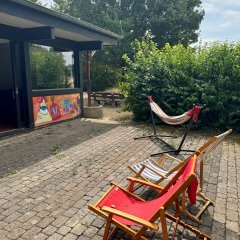 Terrasse mit Liegestühlen, Hängematte und Sitzbank vor einem begrünten Außenbereich.