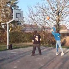 Drei Personen spielen Basketball auf einem Freiplatz.