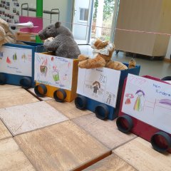 vier gemalte Bilder, die auf einen mit Kisten gebauten Zug kleben, auf denen steht: "Klamotten kaufen", "Zusammen kuscheln", Zusammen kochen" und "Mein Kinderzimmer"
