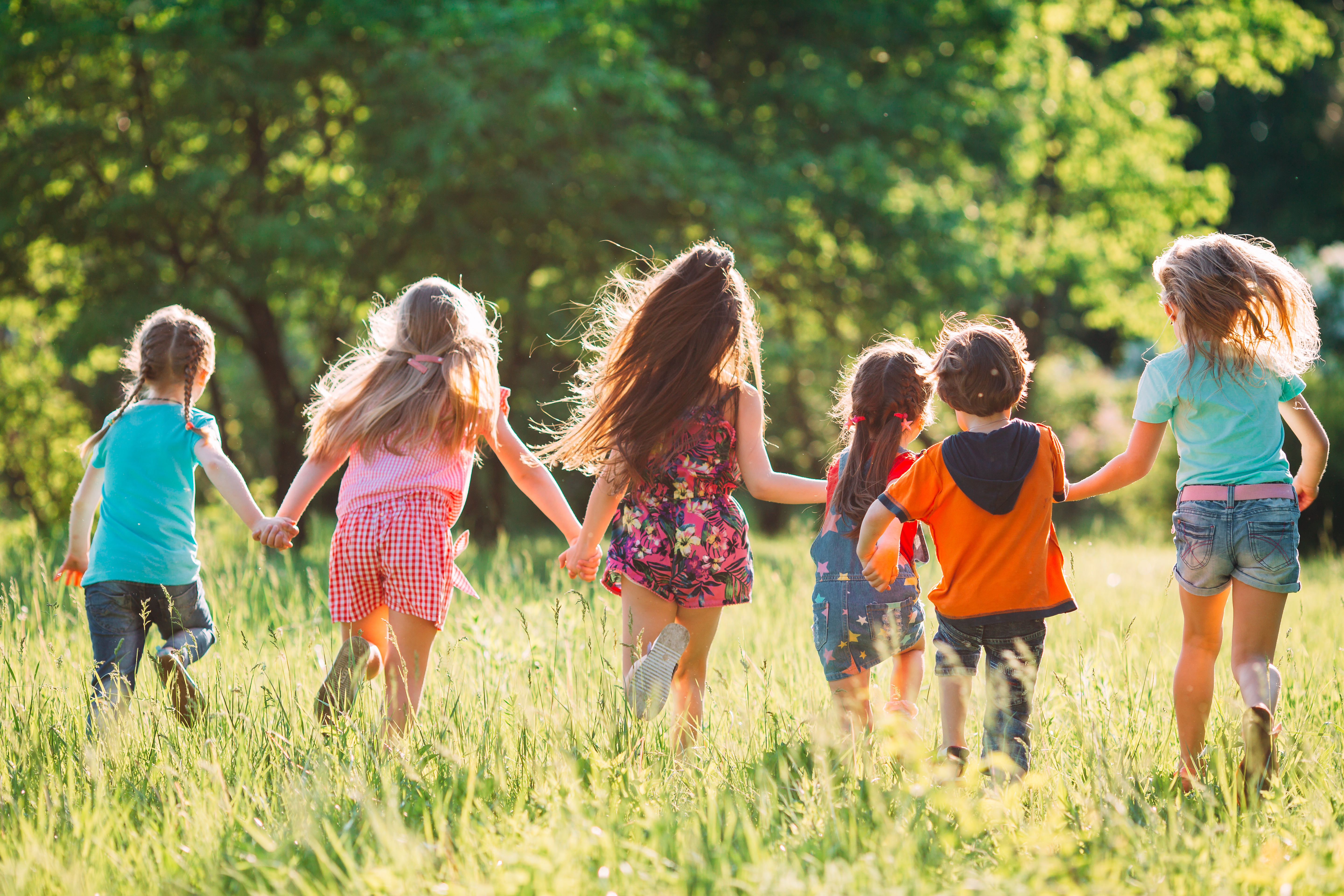 Large group of kids, friends boys and girls running in the park on sunny summer day in casual clothes .