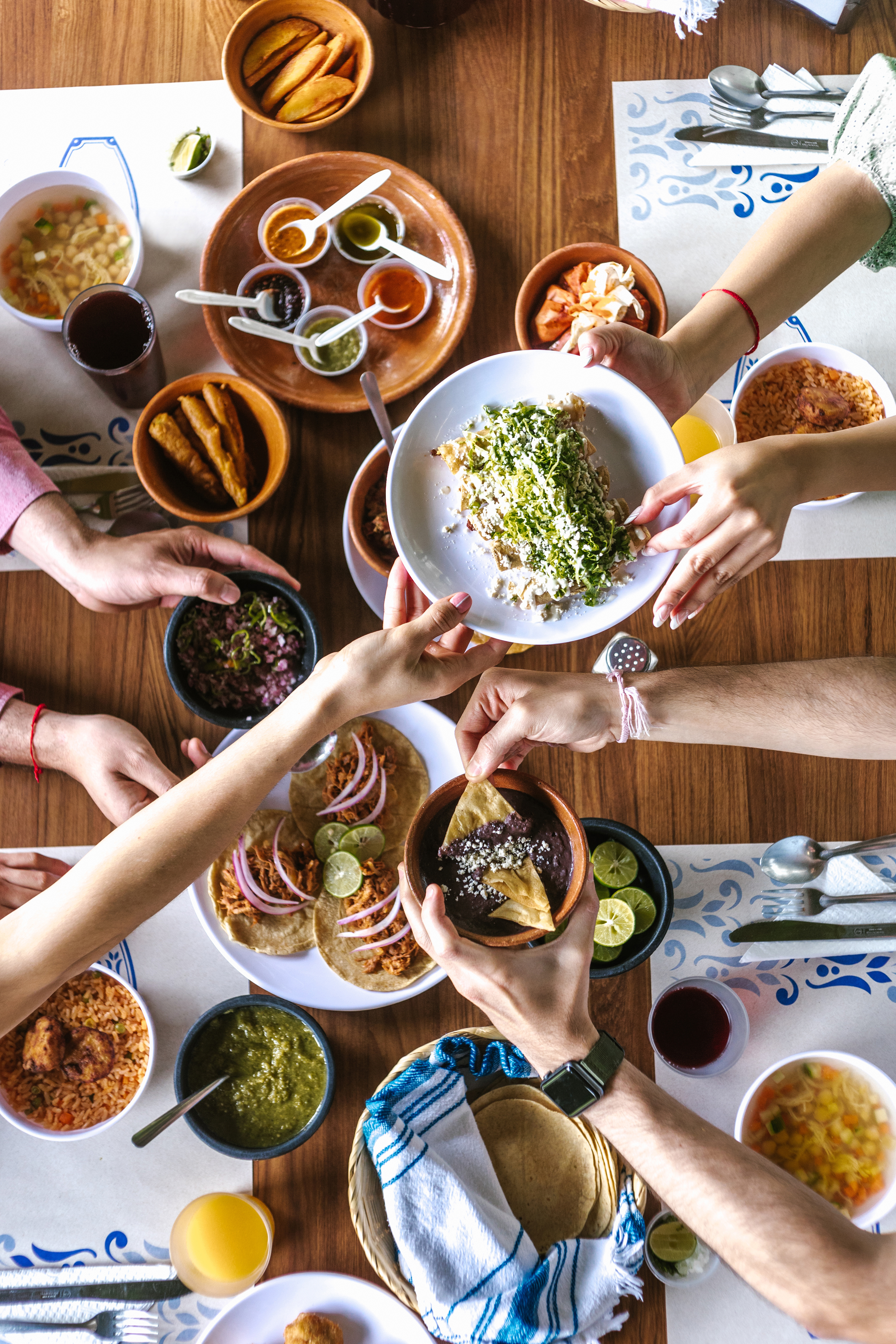Group of friend eating mexican tacos and traditional food, snacks and people's hands over table, top view. Mexican cuisine
