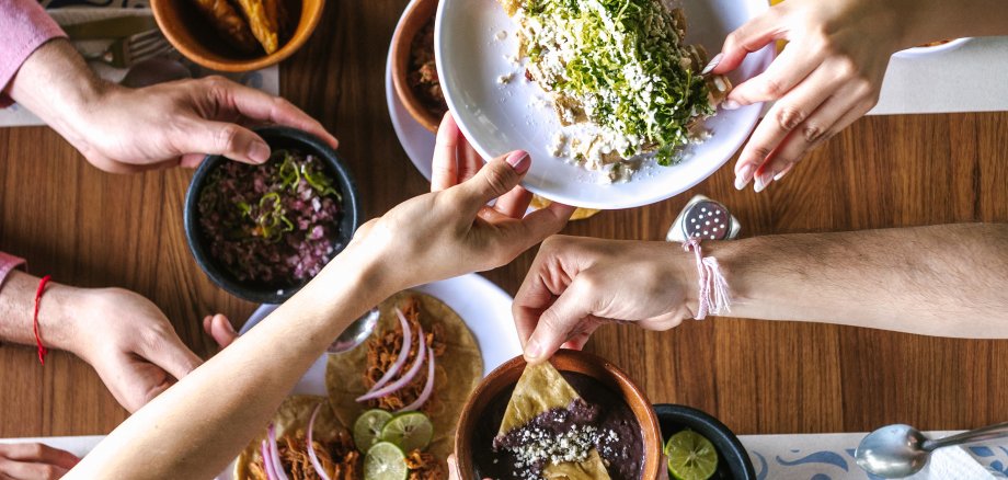 Group of friend eating mexican tacos and traditional food, snacks and people's hands over table, top view. Mexican cuisine