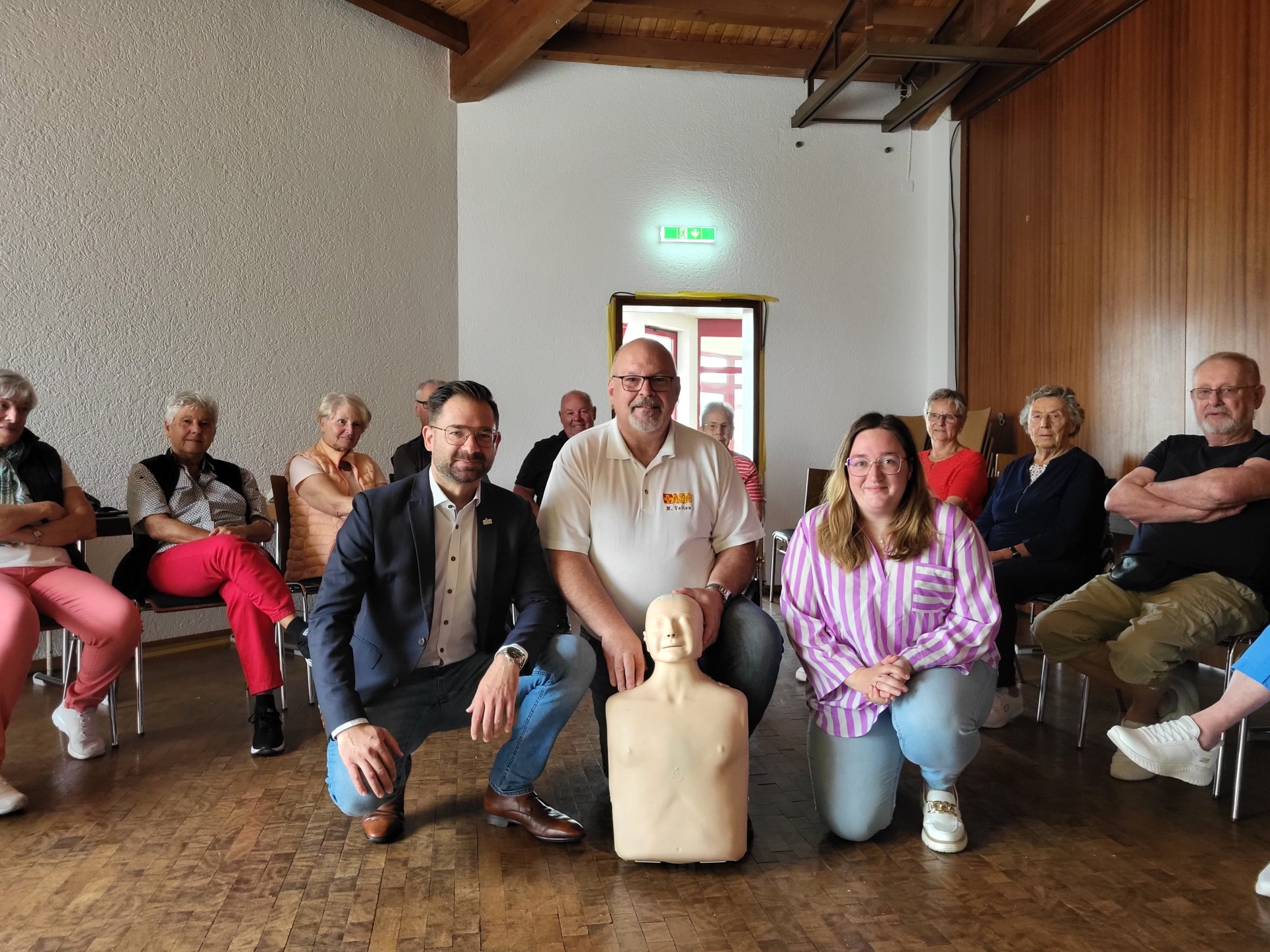 Bild von links nach rechts: Im Kreis der gespannten Teilnehmerinnen und Teilnehmer: Bürgermeister Christian Aßmann, Michael Velten (ASB Westhessen) mit Übungspuppe „Anne“ und Gemeindepflegerin Ricarda Treunert-Paltz