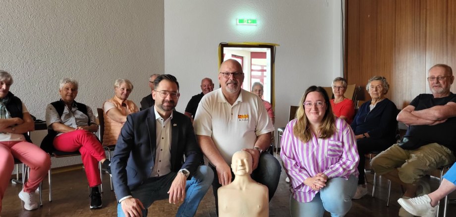 Bild von links nach rechts: Im Kreis der gespannten Teilnehmerinnen und Teilnehmer: Bürgermeister Christian Aßmann, Michael Velten (ASB Westhessen) mit Übungspuppe „Anne“ und Gemeindepflegerin Ricarda Treunert-Paltz
