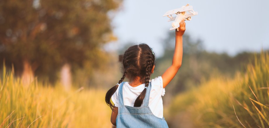 Cute asian child girl running and playing with toy wooden airplane in the field at sunset time with fun Kind rennt und spielt mit Flugzeug