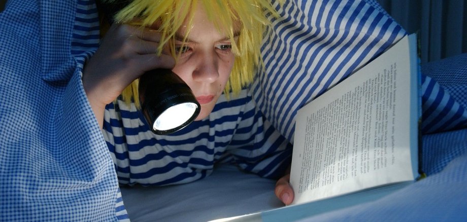 Kind liest unter der Bettdecke mit einer Taschenlampe mit einem Buch