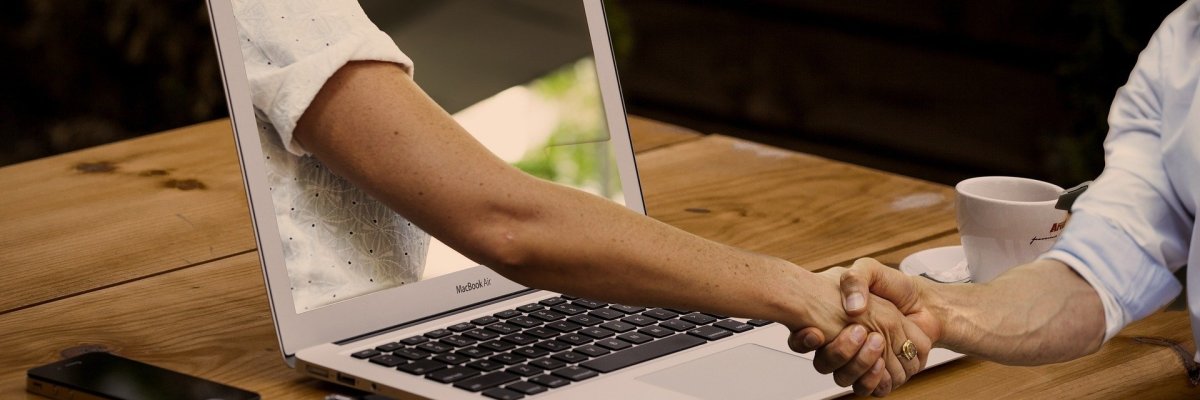 Zwei Personen reichen sich durch einen Laptop die Hände