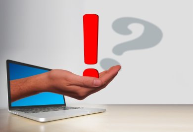 eine Hand, die durch einen Laptop durchgreift und ein Ausrufezeichen auf der Handfläche hat