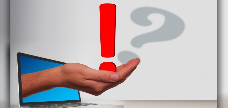 eine Hand, die durch einen Laptop durchgreift und ein Ausrufezeichen auf der Handfläche hat
