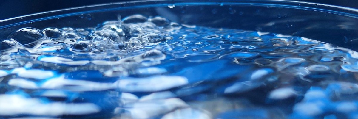 Glas mit Wasser, in das ein Tropfen reintropft